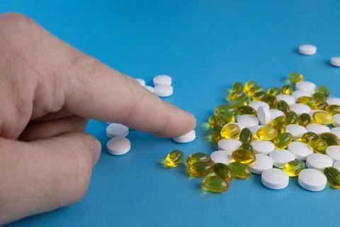 Human finger sorting white tablets and yellow capsules on blue background, Stock Photos