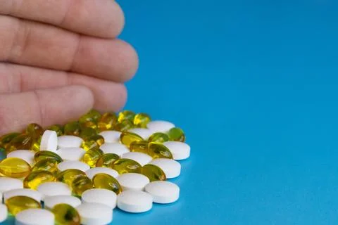 Human finger sorting white tablets and yellow capsules on blue background 스톡 사진