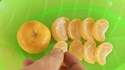 Human fingers picking up a single peeled tangerine segment from a green lea.. Video stock 328674522