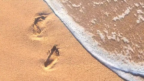Human Footprints on yellow sandy beach washed by sea waves. Two footprints are Stock Footage 302957087