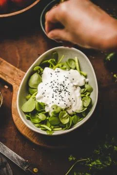 Human hand adding black sesame to fresh green purslane salad Stock Photos