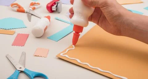 Human hand applying white glue orange paper with scissor stapler Stock Photos
