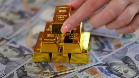 Human hand arranging stack of gold bars on dollars banknotes Stock Photos