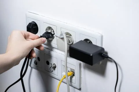 Human hand carefully plugging a black power cable into a white wall socket .. Stock Photos