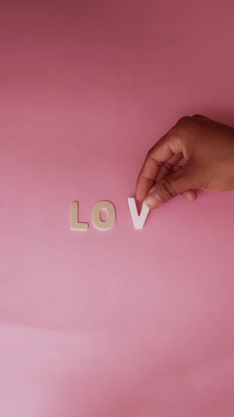 Human hand composing the word love with wooden letters on pink background Video stock 326364426