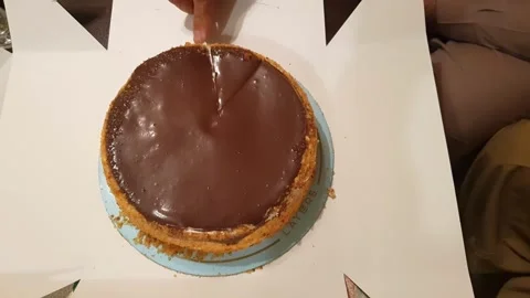 Human hand cutting chocolate and caramel milk cake on cake paper packing. Stockbeeldmateriaal 345277196