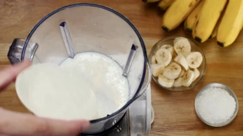 Human hand dropping crystal sugar in a mixer grinder with banana and milk - S... Stock Footage 154154419