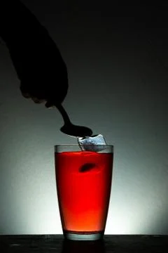 Human hand dropping Ice cube into a glass of juice Stock Photos
