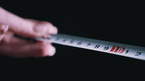 Human Hand Extending Metal Measuring Tape Against Dark Black Background Видео 332666967