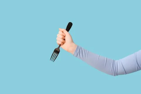 Human hand holding black fork on blue background, kitchen utensil for eating  Stock Photos