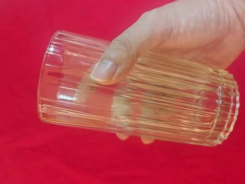 Human Hand Holding Empty Transparent Drinking Glass Cup in red background a Stock Photos
