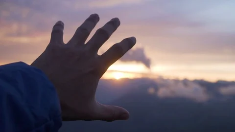 Human hand holding in front of sun flare during colorful purple sunset Stock Footage 129610500