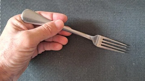 Human hand holding shiny silver metal fork over patterned mat Stock Photos