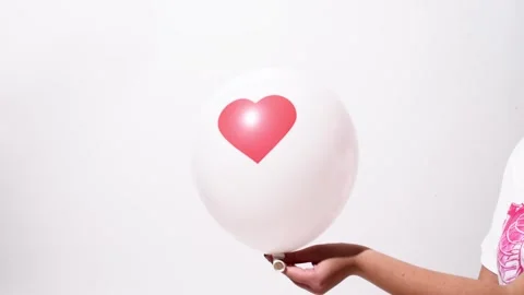 Human hand holding white ballon with print of heart on white background, studio Stock Footage 244060357