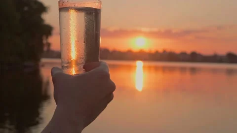 Human hand holds misted glass of water at sunset by the river Stock Footage 201617705
