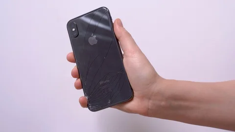 Human hand holds smartphone iPhone X with broken back glass Stock Footage 129793282
