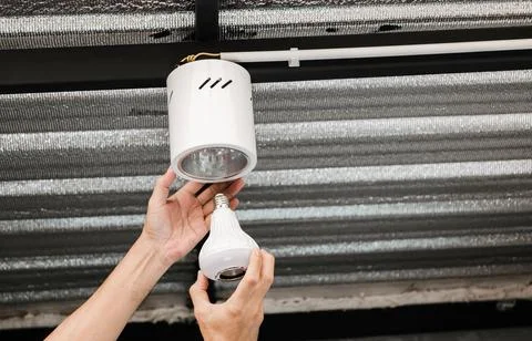 Human hand is installing an LED light bulb in a circular ceiling lamp. Stock Photos