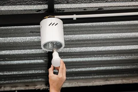 Human hand is installing an LED light bulb in a circular ceiling lamp. Stock Photos