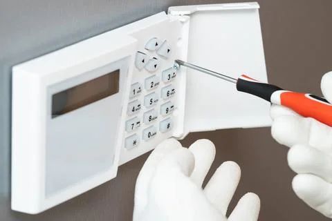 Human hand installs a security system on a gray wall. Stock Photos