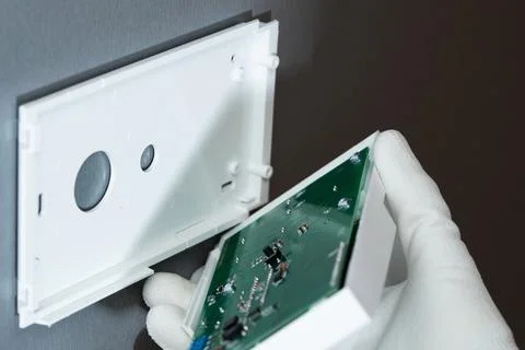 Human hand installs a security system on a gray wall. Stock Photos