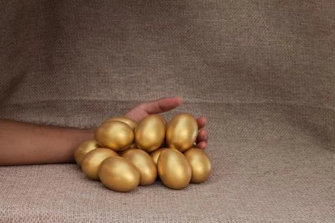 Human hand lay down closed to heap of golden egg Stock Photos