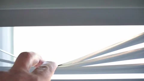 Human hand lifting window blinds to reveal bright daylight. Stock Footage 338428914