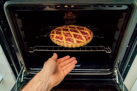 Human hand loading lingonberry pie pan into oven on baking plate Stock Photos