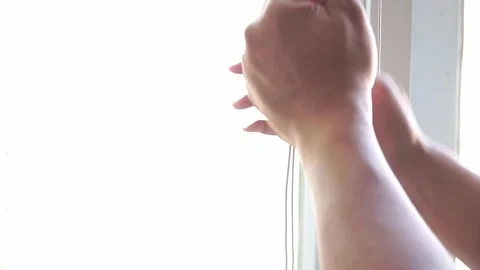 Human hand operating a window blind string to allow natural sunlight indoors. Stock Footage 338191014