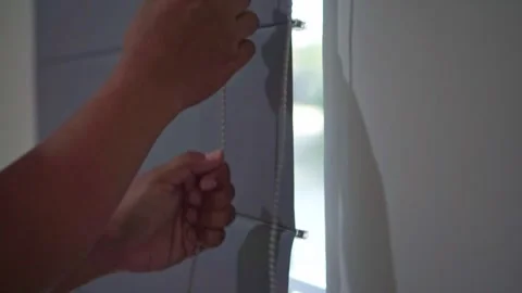 Human hand operating a window curtain chain to allow sunlight indoors. Stock Footage 341379928