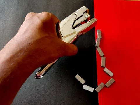Human hand picking up big stapler. Isolated on red background. Stock Photos