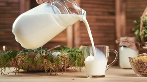 Human hand pour fresh appetizing milk from jug into glass mug serving table for Vídeos de archivo 165866125