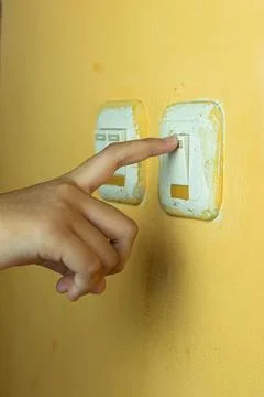 A human hand pressing a light switch on a yellow wall Stock Photos