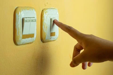 A human hand pressing a light switch on a yellow wall Stock Photos