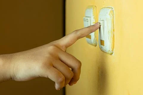 A human hand pressing a light switch on a yellow wall Stock Photos