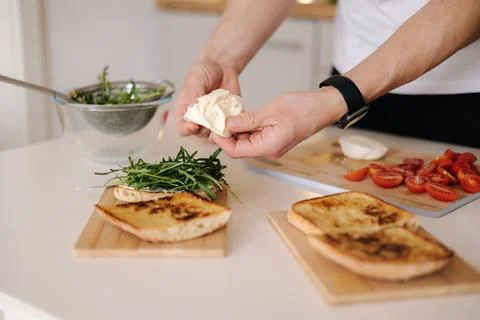 Human hand put piece of mozzarella on sandwich with arugula. Classic Italian Фото