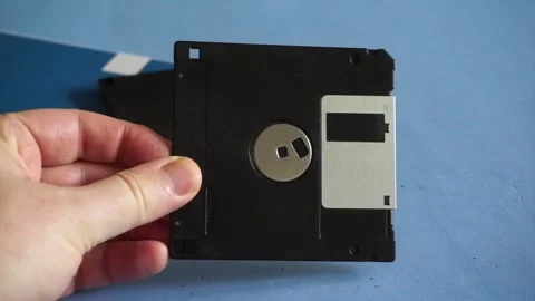 Human hand putting several vintage 3.5 inch floppy disks on a blue desk next to Stock Footage 340118460