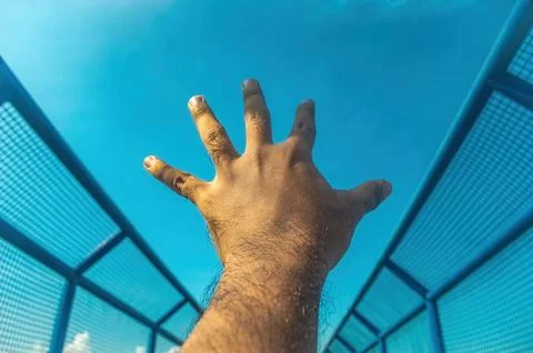 A human hand reaches dynamically upwards toward a vast, clear blue sky, fra.. Foto stock