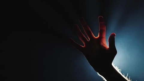 Human hand reaching up towards soft light beams in dark environment. Vidéo 335866632