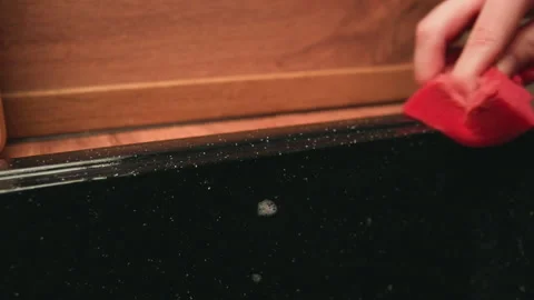 Human hand scrubbing worn black suitcase edge with red sponge under warm light Stock Footage 343535097