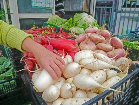 A human hand selects vegetables and fruits from a box at the market Stock Photos