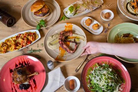 Human hand serving a plate over a variety of meat and fish meals. Buffet top  Stock Photos