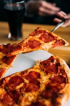 Human hand serving a slice of pepperoni pizza Stock Photos