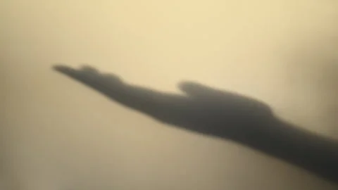 Human hand shadow reaching across warm beige wall in golden sunset light Stock Footage 340084189