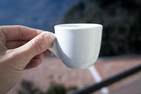 Human hand with small white empty cup espresso coffee in bright sunlight. Sky Stock Photos