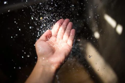 Human hand in sunlight under falling water. Stock Photos