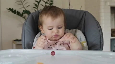 The human hand throwing a berry on the baby's table, which he takes and puts in Stock Footage 170468748