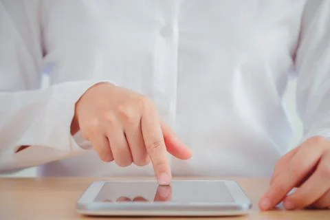 Human hand touching the screen of a tablet which is placed on the office desk Stock Photos