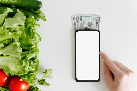 Human hand touching smartphone mockup, eco vegetables and money on table, t.. Stock Photos