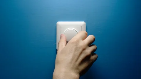 Human hand turns dimmer button on a blue wall slowly Stock Footage 125597723