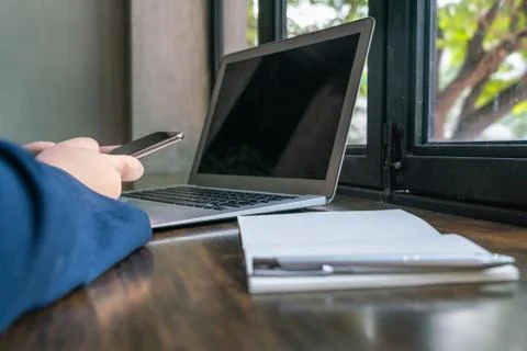 Human hand using cellphone next to laptop and notebook Stock Photos